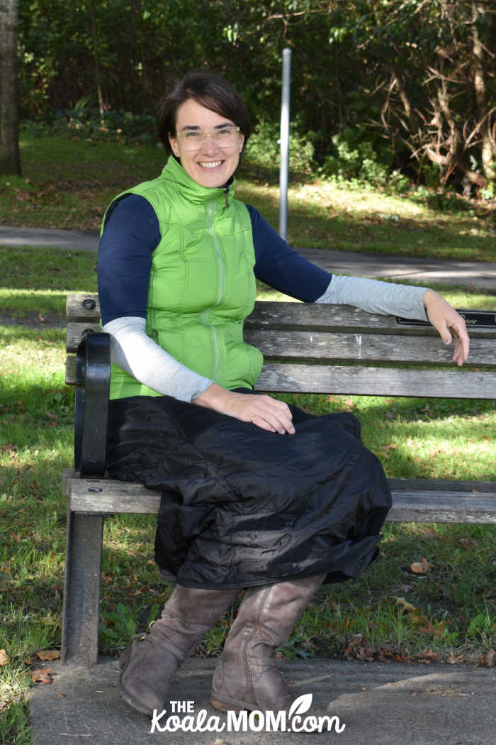 Happy woman on a park bench wearing a thermal wrap around her lower body to stay warm.