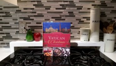 The Vatican Christmas cookbook, resting on a stove with salt and pepper shakers and three canisters labeled garlic, pasta and utensils.