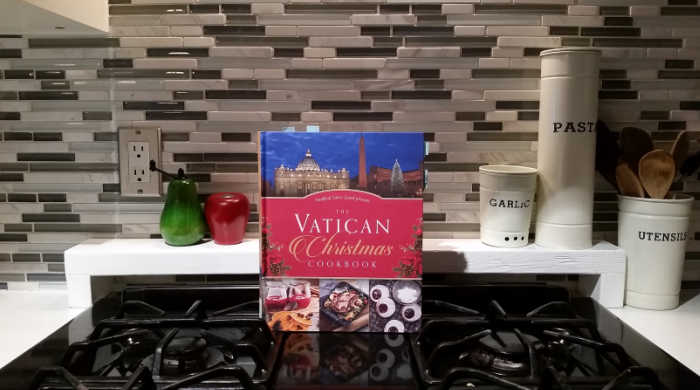 The Vatican Christmas cookbook, resting on a stove with salt and pepper shakers and three canisters labeled garlic, pasta and utensils.