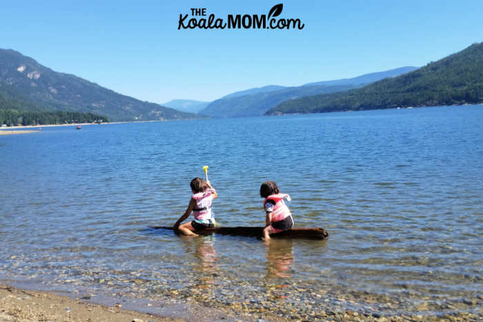 Kids wearing their PFDs and playing in a lake with a floating log.