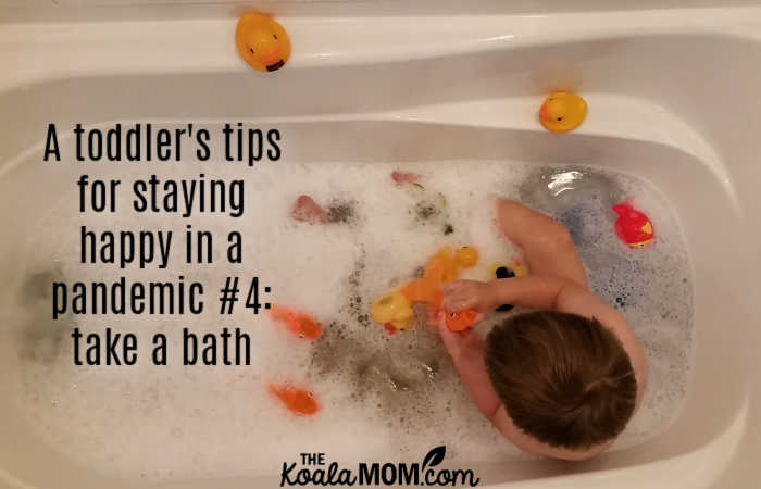 A toddler's tips for staying happy in a pandemic #4: take a bath (like this toddler playing with his goldfish and rubber duckies in a buble bath).