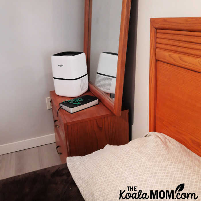 An Okaysou air purifier sits on a bedroom nightstand.