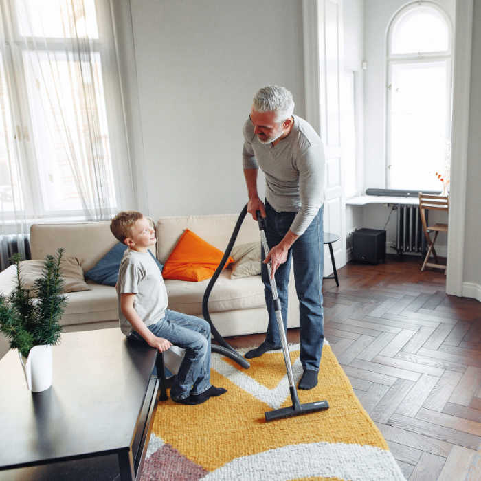 Dad vacuuming the living room while chatting with his son.