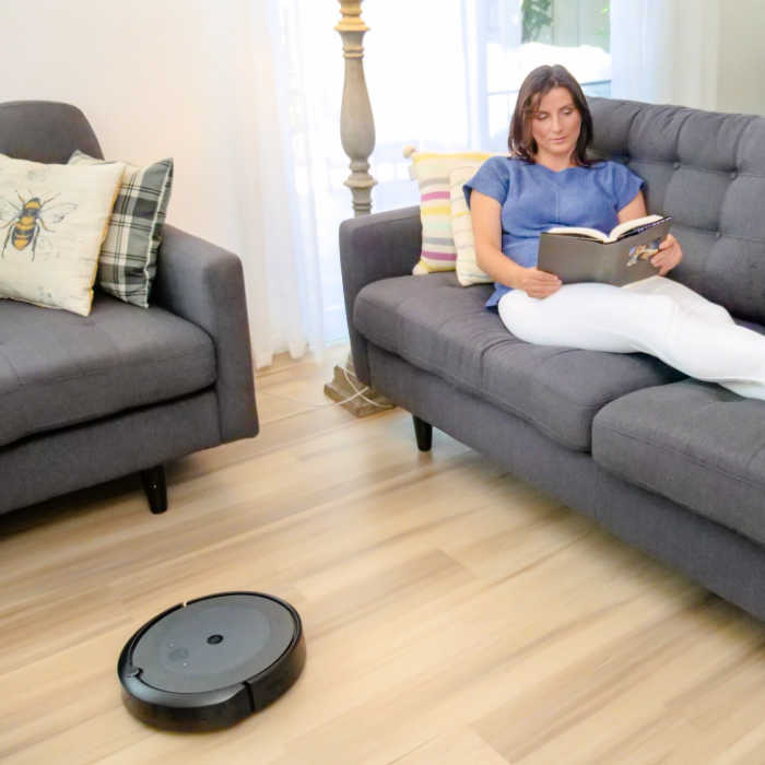 Mom reading while a robot vacuum cleans her hardwood floor.