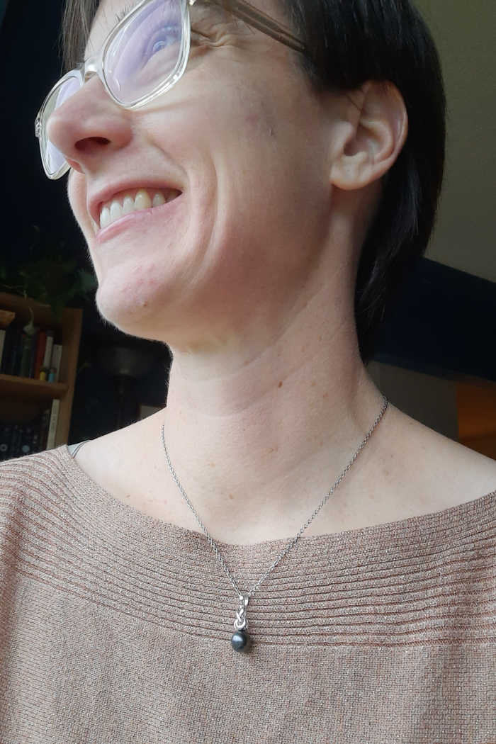 Woman in a sparkly gold top wearing a single black pearl pendant on a silver chain.