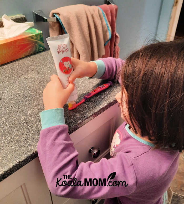 Girl in pajamas puts Green Beaver kids strawberry toothpaste on her toothbrush.