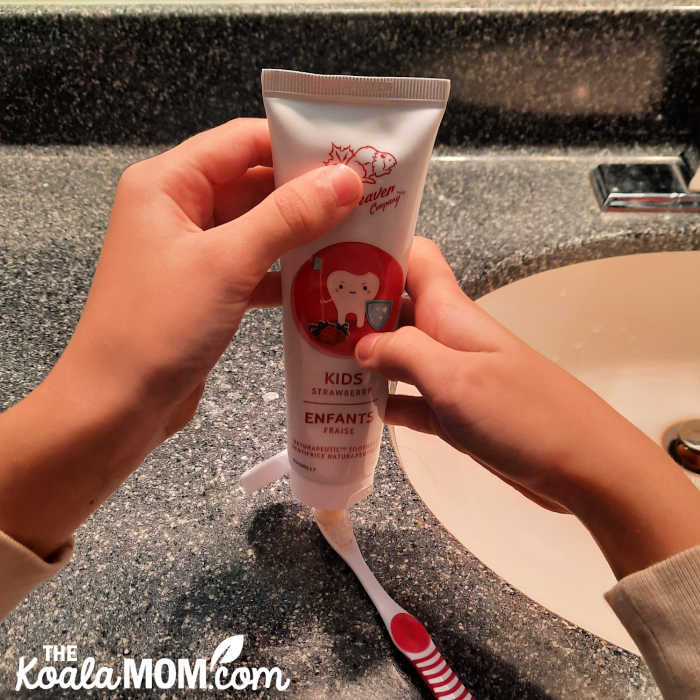 Child putting Green Beaver kids strawberry toothpaste on her toothbrush.