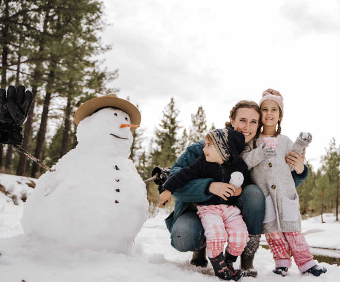 Mom and two kids posing with their snowman.