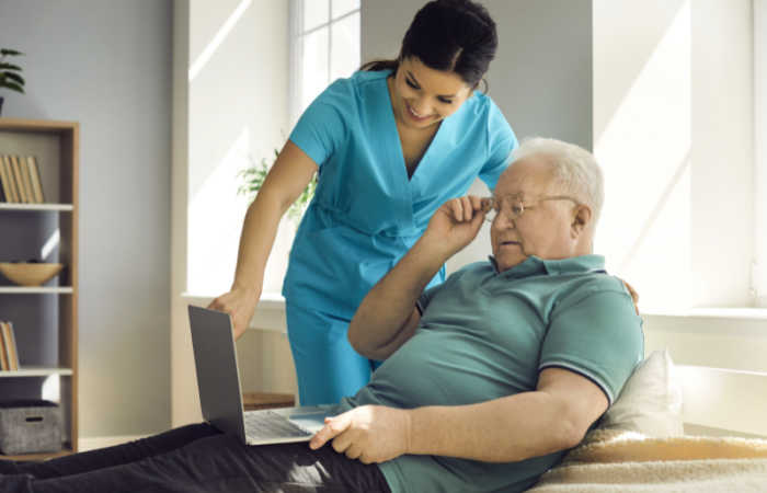 Home care nurse helps a senior gentleman with his laptop.