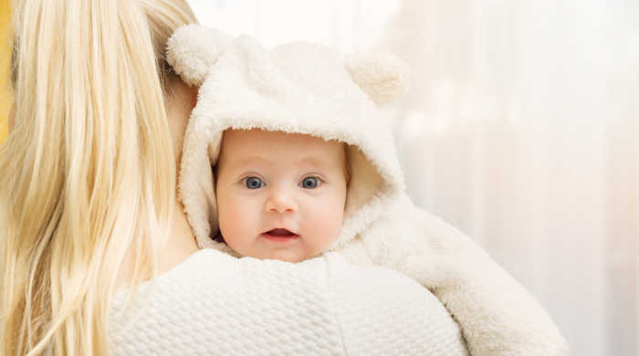 Baby on mom's shoulder, wearing a hoodie with bear ears. Source: ronstik/Shutterstock.com