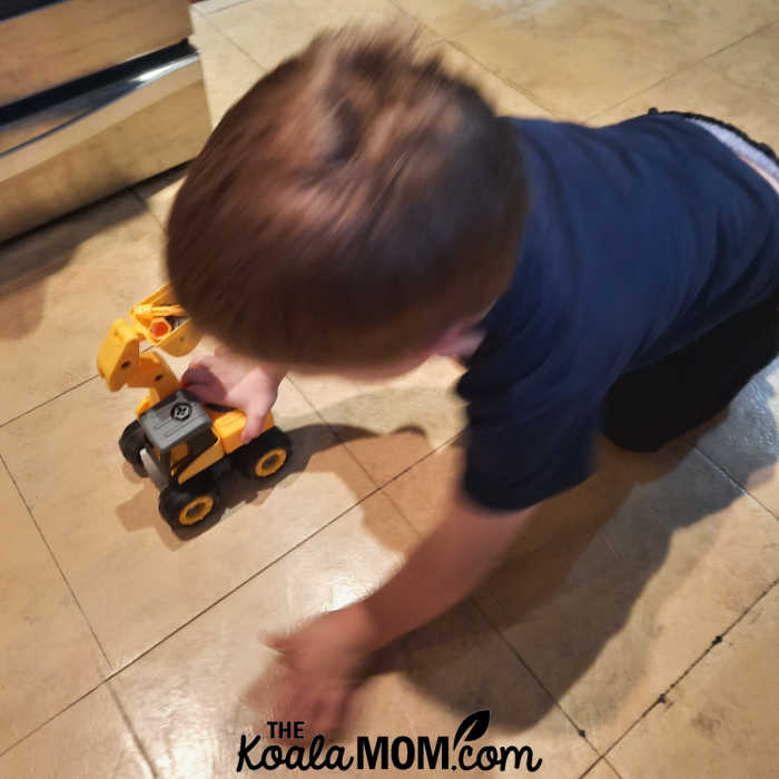 Boy pushes his plastic digger toy along the floor.