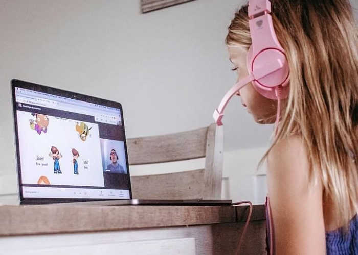 Girl wearing pink headphones learns Spanish online.