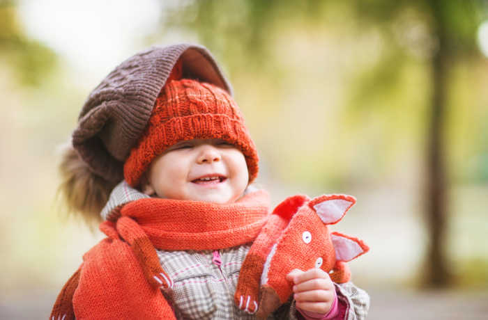 Laughing child bundled in an orange fox scarf, wearing two knit hats. Source: phBodrova/Shutterstock.com
