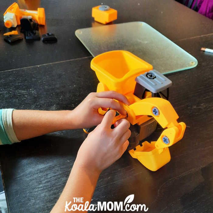 Girl screws digger arm onto her construction toy.