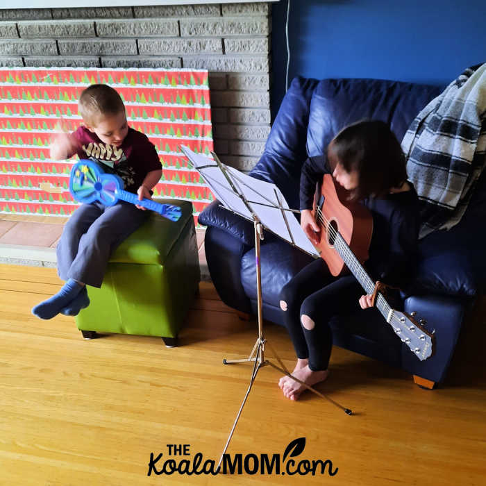 An 8-year-old and a 4-year-old play guitar together.