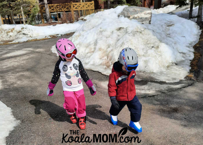 6-year-old and 4-year-old walk to ski lift together in their ski gear.