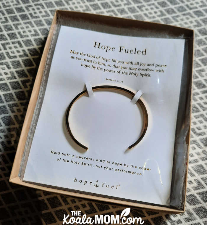 Gold "fueled bracelet" in box with card reading, "Romans 15:13 “ May the God of hope fill you with joy and peace as you trust in him, so you may overflow with hope by the power of the Holy Spirit.”