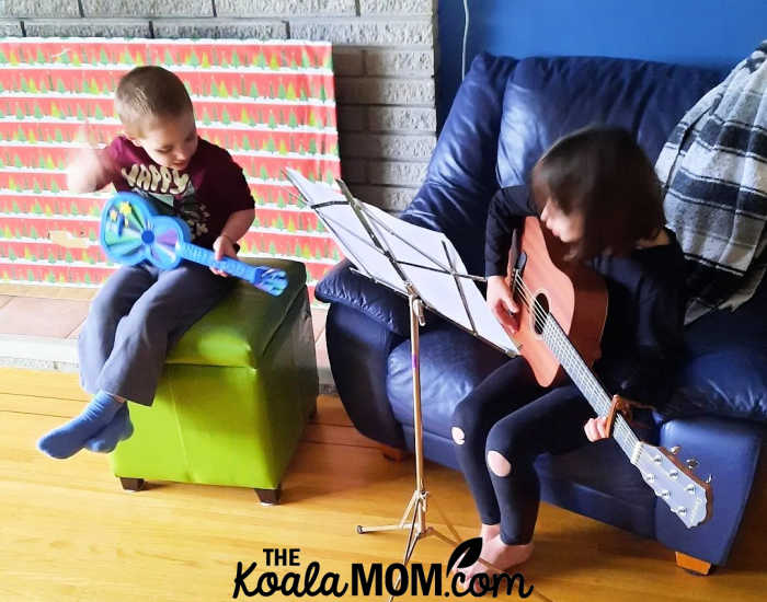 A 8-year-old and 4-year-old sibling play their guitars together.