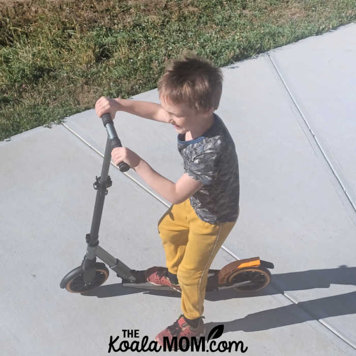 Blonde boy rides his McLaren scooter.