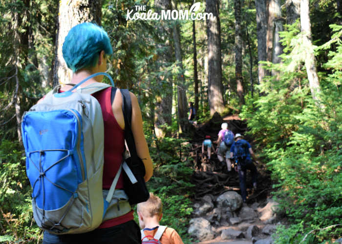 Mom carrying a large blue hiking daypack while following her toddler on the trail.