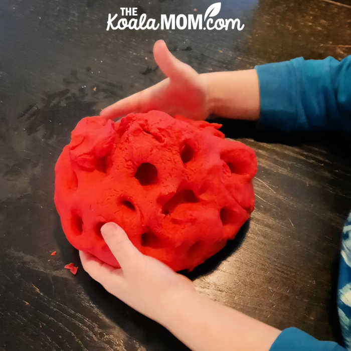 Little boy playing with a ball of red play dough he made with his mom.