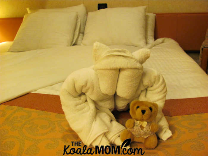 Folded towel baboon sitting on cruise ship room bed with a teddy bear.