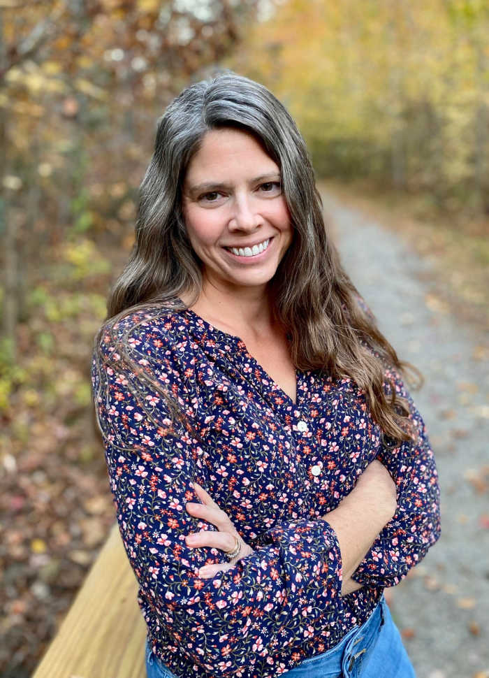 Ginny Kochis, author of Blink and We'll Miss It, poses on a path in the woods.