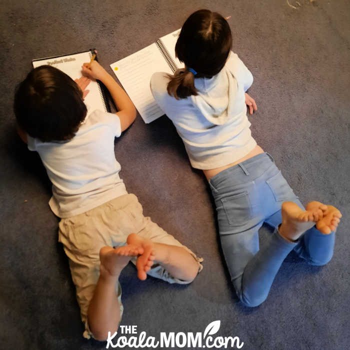 Two homeschooling sisters work on their science together while sprawled on the floor.