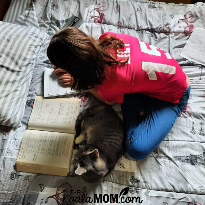 Homeschooler doing her math lesson on her bed, with her cat cuddling close.