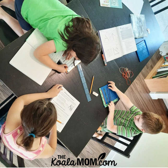Three homeschool siblings working together at the dining room table.