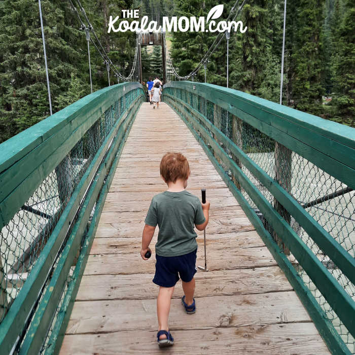 3-year-old boy walks over bridge to go mini golfing with his sisters.