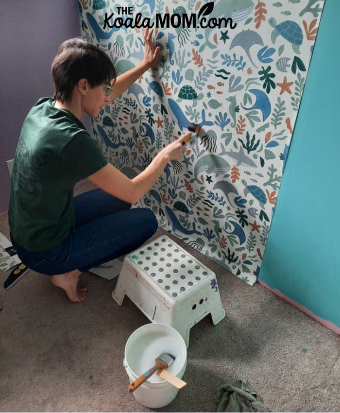Using a wallpaper roller to smooth ocean-themed wallpaper onto a blue wall.