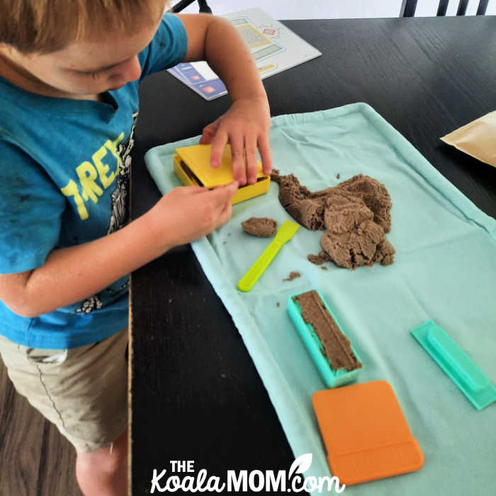 4-year-old boy plays with kinetic sand on a wipe clean mat.