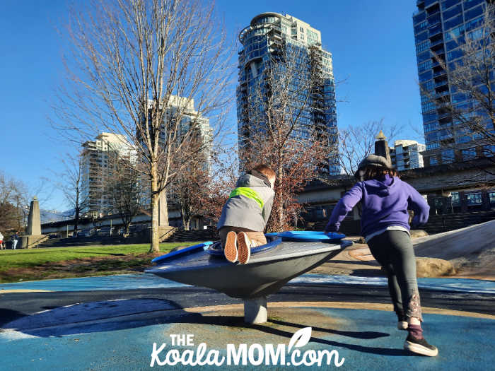 Two kids play on a merry-go-round at Vancouver's Science World playground. Photo by Bonnie Way.