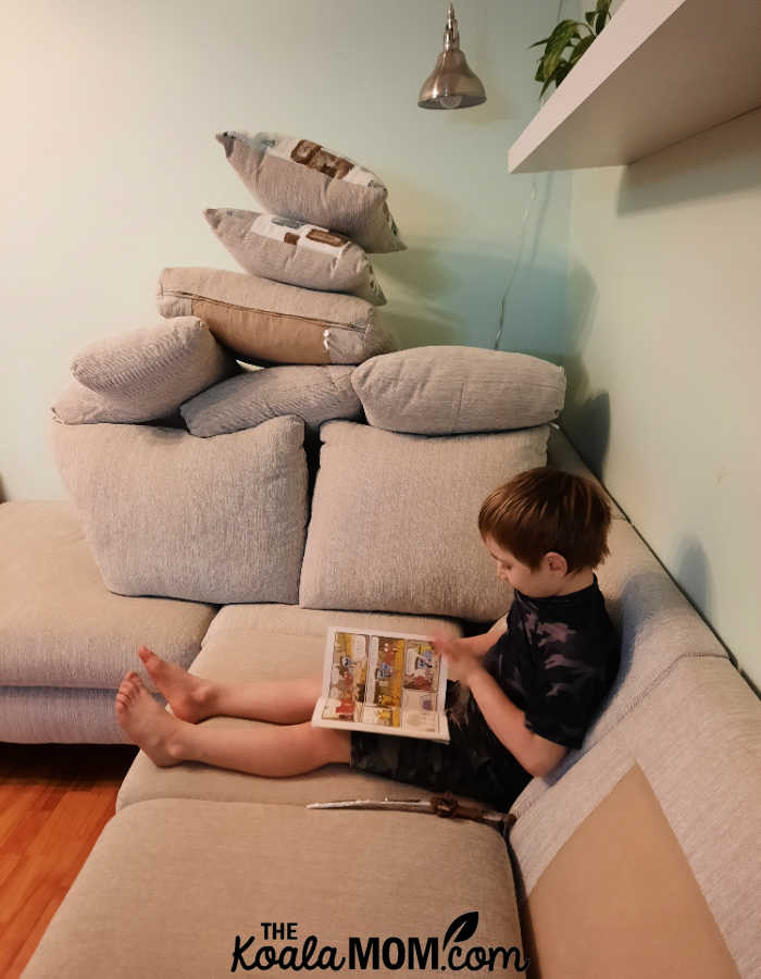 Boy reading on a sectional with the cushions piled up in a fort behind him. Photo by Bonnie Way.