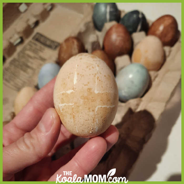 Mom holds an Easter egg with a cross on it above a carton of naturally-dyed Easter eggs. Photo by Bonnie Way.