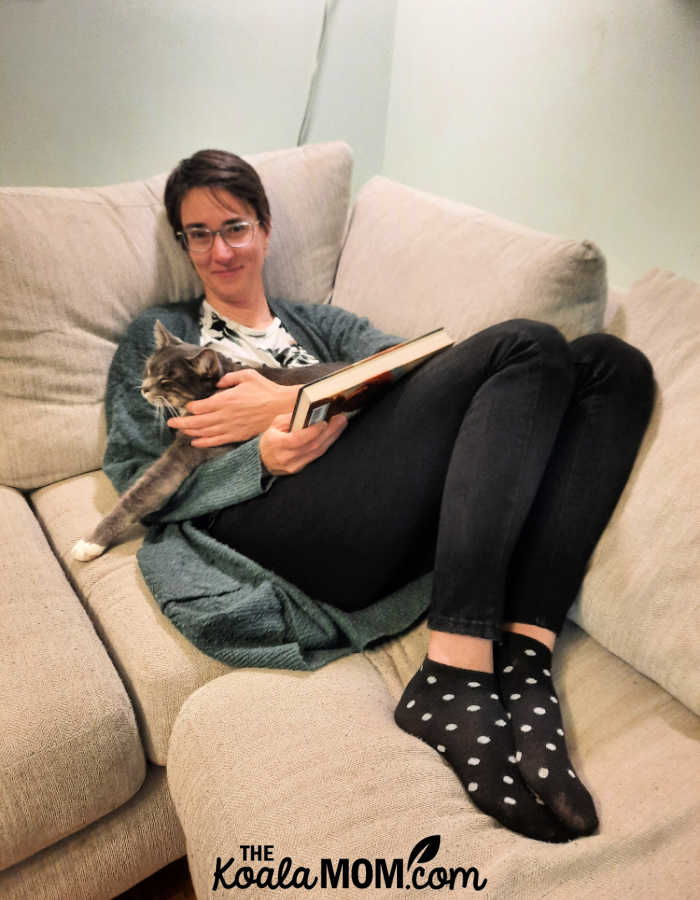 Woman holding a cat and a book on a comfy sectional.