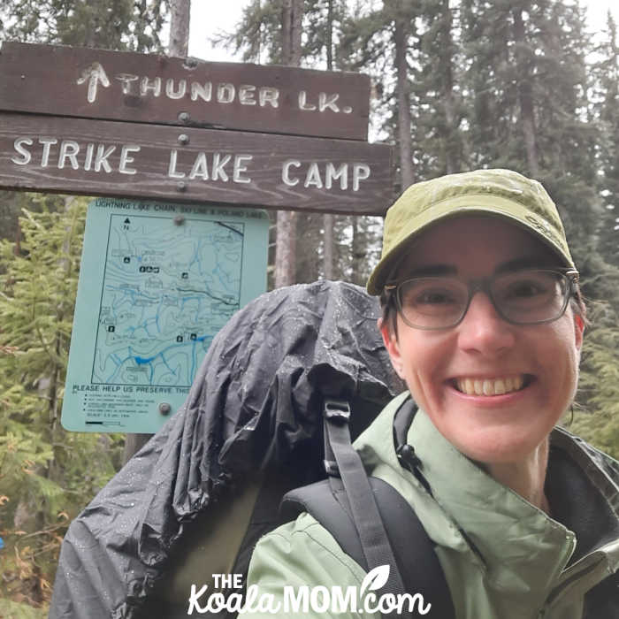 Bonnie takes a selfie with the sign and map for the Strike Lake Camp.