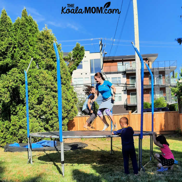 Two kids bouncing on a trampoline outdoors while two kids wait their turn. Photo by Bonnie Way.