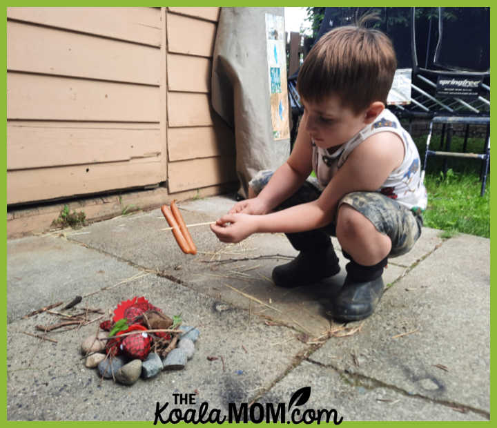 Boy pretends he's cooking his pepperoni sticks over a "campfire" made of a circle of rocks, twigs, and his red stuffed lizard as the fire. Photo by Bonnie Way.