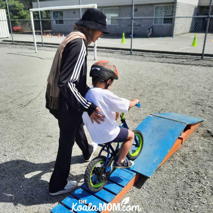 Pedalheads instructor helping boy ride his bike over an obstacle. Photo by Bonnie Way.