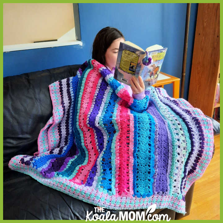 Teenager sits under a stripey crocheted calendar blanket. Photo by Bonnie Way.